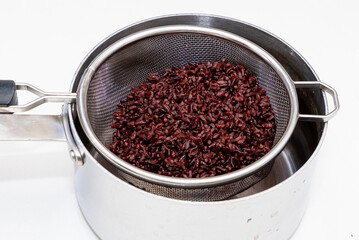Cooked whole grain brown rice inside metal strainer in kitchen