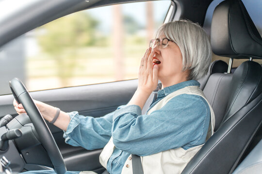 Elderly/senior woman yawning due to feeling sleepy while driving a car