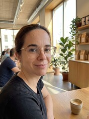 Woman with glasses sitting at a table in a cafe with a cup of coffee