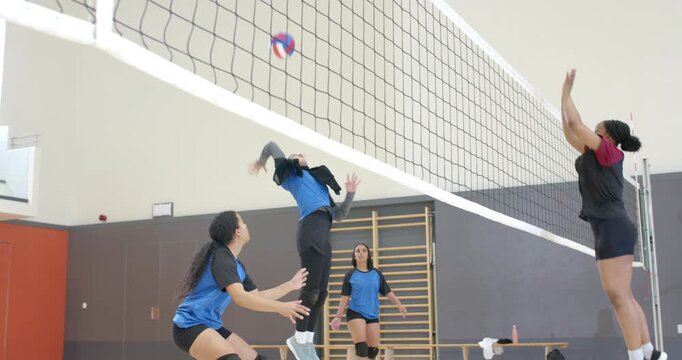 Diverse female volleyball trio launching block on opponent spiking at court net celebrating point