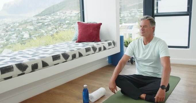 Mature man gazing at hillside, shifting into meditating on green mat to center self, copy space