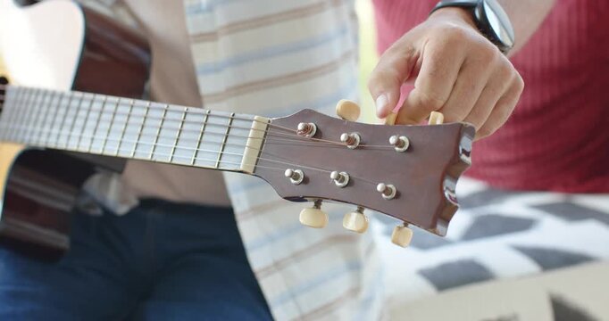 Right hand is reaching, turning guitar tuners on couch while partner holding guitar, checking pitch