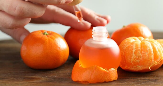 Woman applying tangerine essential oil onto her fingernail cuticles at wooden table, closeup
