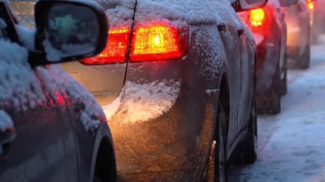 Commuter cars stuck in heavy traffic during snowy winter blizzard at dusk