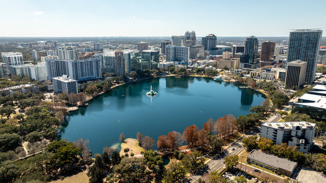 A sweeping drone view of Lake Eola Park highlights the downtown Orlando skyline reflected across the lake.