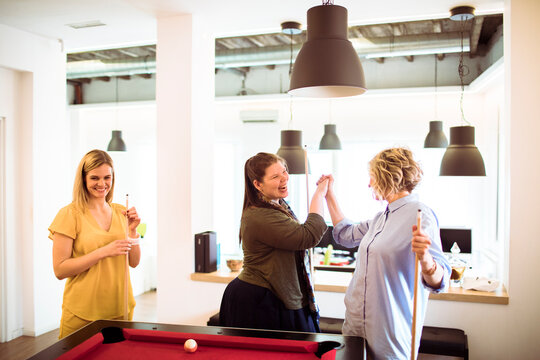 Coworkers playing billiards and high-fiving in a modern office break room