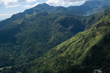 Obraz premium Winding mountain road on the slope of Ella Rock, Sri Lanka, seen from Little Adam’s Peak. Lush greenery, scenic depth and tropical highland landscape create an inspiring travel scene.