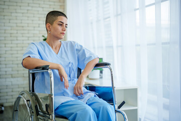 Obraz premium Calm patient hospital wheelchair medical gown short hair natural light window curtain brick wall healthcare recovery rehabilitation seated indoors clinical sterile pensive contemplative solitude