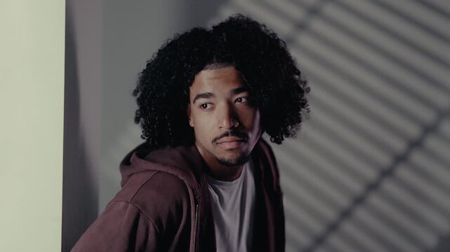 Portrait of a thoughtful young African-American man with curly hair, conveying a sense of worry and contemplation in a dimly lit setting