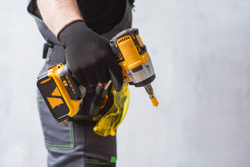 Professional construction worker in gloves holding powerful cordless impact driver power tool against grey background.