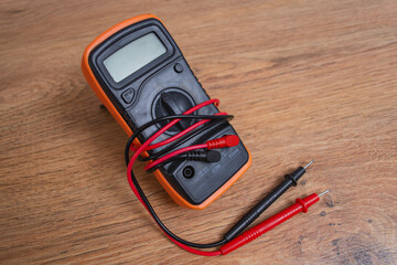 Orange digital multimeter with test probes on wooden background for electrical measurement and diagnostics.