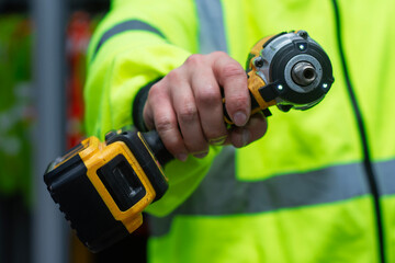 Construction worker in high visibility safety jacket holding professional cordless impact wrench power tool.