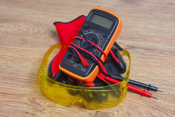 Digital multimeter with protective yellow glasses and work gloves for electrical safety and testing.
