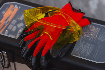 Personal protective equipment with yellow safety goggles and red work gloves on black toolbox.
