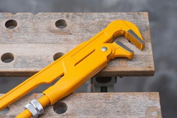 Professional yellow adjustable pipe wrench lying on wooden workbench in workshop for plumbing repair work.