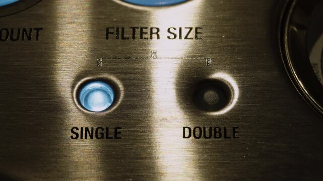 Extreme close up of a brushed metal espresso machine interface as the blue indicator light switches from single to double filter size.