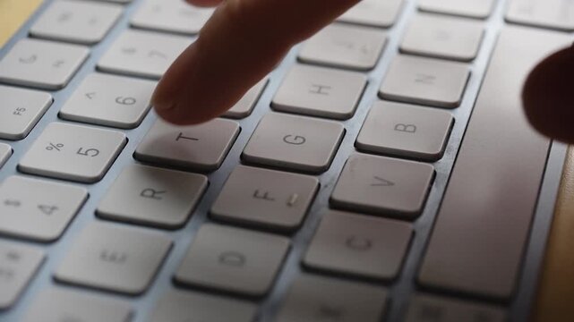 Macro shot of a single hand typing on a silver computer keyboard. Ideal for technology, remote work, and digital accessibility concepts.