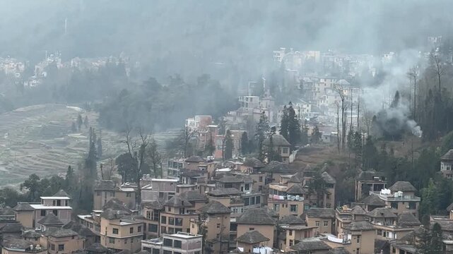 A serene 1080p horizontal static shot capturing a traditional Chinese hillside village. The footage features ancient residential houses overlooking lush agricultural terraced fields, with ethereal whi