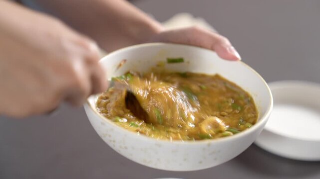 Close-up of Whisking Egg into Savory Thick Fish Maw Soup in a Ceramic Bowl