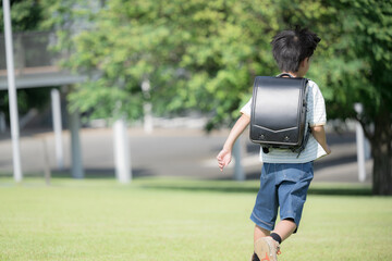 学校の校舎を背景に校庭でランドセルを背負って走る少年の(男の子)男子後ろ姿で顔無しの全身
