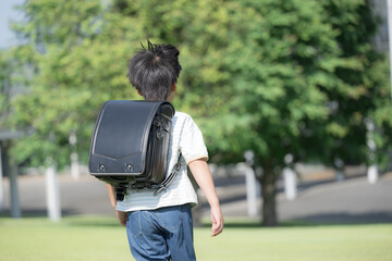 学校の校舎を背景に校庭でランドセルを背負って走る少年の(男の子)男子後ろ姿で顔無しの全身