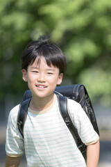 学校の校舎を背景に校庭でランドセルを背負って走る少年の(男の子)男子の笑顔のクローズアップ