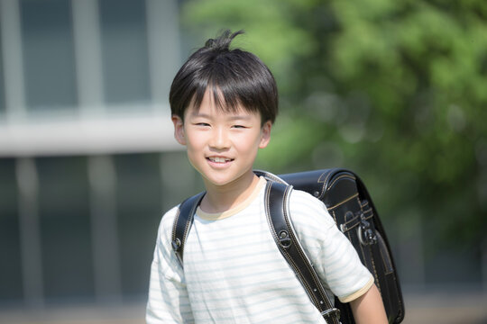 学校の校舎と緑を背景に校庭でランドセルを背負って走る少年の(男の子)男子の笑顔のクローズアップ