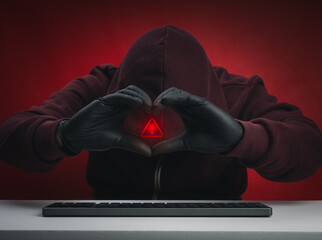 Red hooded scammer forming heart shape with hands over keyboard, Romance scam, fake love, online...