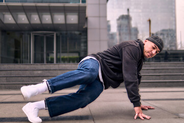 Fit young adult enthusiastically break dancing, spinning on the floor, dressed in jeans, urban clothing, and a cap. Lots of attitude, movement, and good energy. Street dance, freestyle, modern dance.