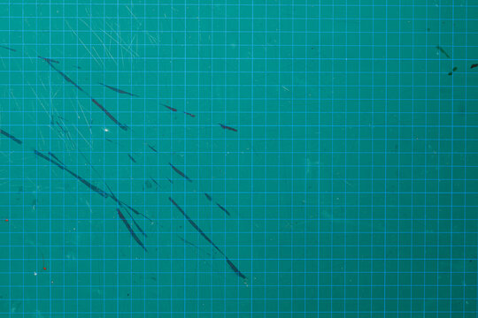 Textured green cutting mat with grid pattern, scratches, and abstract marks. Perfect for backgrounds, textures and craft
