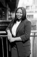 Smiling businesswoman leaning on railing in urban setting, monochrome portrait
