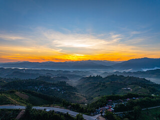 A winding asphalt road stretches through rolling hills with lush greenery, overlooking a valley blanketed in morning fog under a beautiful sky. This scenic landscape conveys freedom