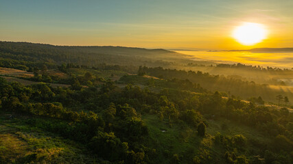 A breathtaking sunrise casts warm golden light over a mist-covered forest and rolling hills, creating a serene and atmospheric landscape scene. Ideal for themes of nature, tranquility © Narong Niemhom