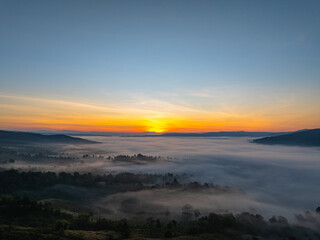 Obraz premium An aerial cinematic sunrise showcasing vibrant sky colors above a fog-covered valley, creating a serene and inspiring nature travel atmosphere. Brilliant Sunrise Painting the Sky Over the Valley