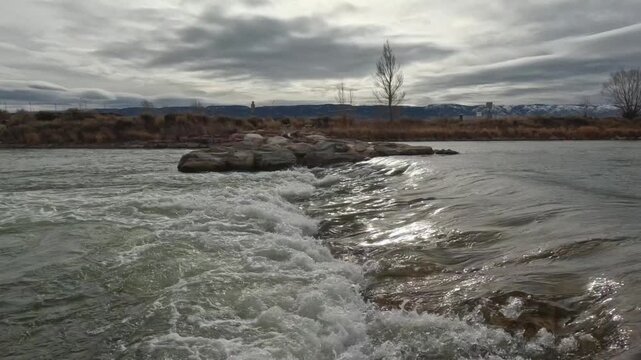 North Platte River in Casper Wyoming has a strong current. Over cast sky, with the sun peaking through the clouds, has glare on the smooth water.