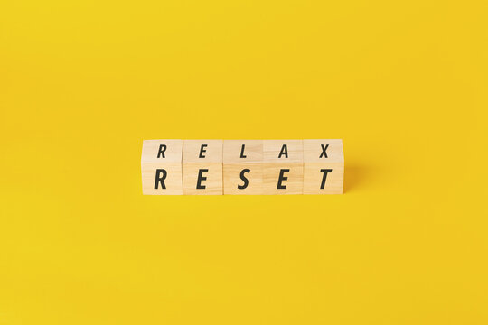 Wooden blocks on a vibrant yellow background displaying "RELAX" and "RESET." Perfect for content about mental health, stress relief, work-life balance, and fresh starts in wellness and business.