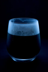 A single stemmed clear glass cup filled with dark liquid and condensation trickling down its side isolated on a black background