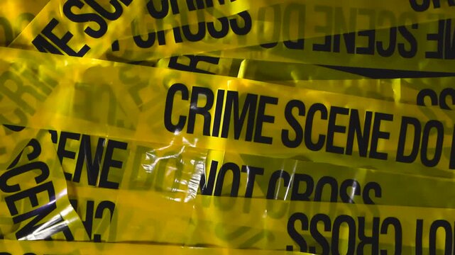 Studio close up of layered yellow forensic barrier tape as the camera lifts upward, revealing bold warning text, strong shadows, and vibrant color under directional lighting.