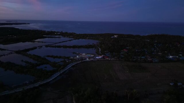Low drone pass skimming rice fields beside a rural road as warm sunset light spreads across Anda countryside.
