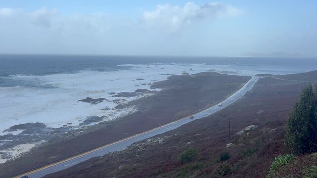 Cars driving along a road with the rough sea in the background in Galicia