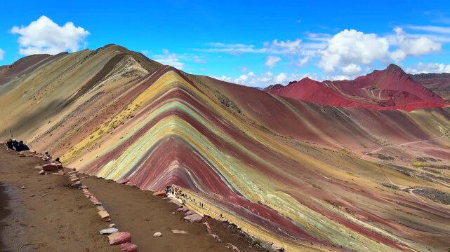 View of Rainbow Mountain Vinicunca Peru Per&uacute; trail morning blue sky Monta&ntilde;a de Siete Colores Palccoyo Peruvian Andes Red Valley striped hills seven colored Cusco Region nature landscape pan right