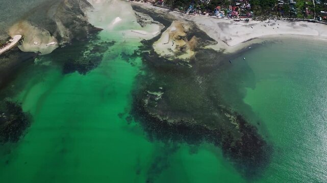 Smooth side glide aerial following Tondol Beach shoreline with crystal-clear water, exposed sandbars, and calm coastal scenery.