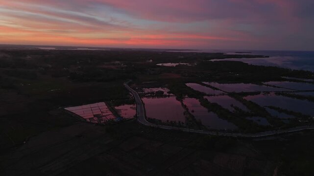 Sunset aerial showing a rural road in silhouette against glowing skies and expansive rice fields in Tondol.