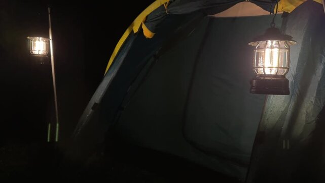 Cozy camping tent illuminated by warm lanterns on a rainy night, highlighting outdoor adventure, nature exploration, travel, relaxation, and tranquility for a memorable wilderness experience.