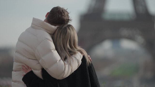 A couple is seen hugging in Paris France with the Eiffel Tower in the background The romantic embrace captures a moment of love and togetherness during their vacation The back view of the loving pair 