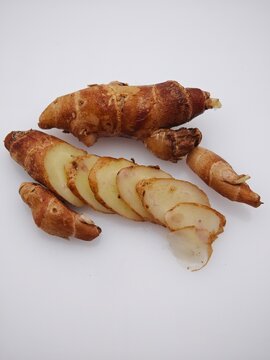A high-angle macro shot of fresh Kaempferia galanga (aromatic ginger) rhizomes, featuring one whole root and several thin slices on a clean white background.