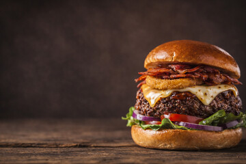 Brioche bacon cheeseburger with onion ring and copy space on dark background
