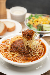 伸びる麺をフォークで持ち上げたミートソースのスープパスタ