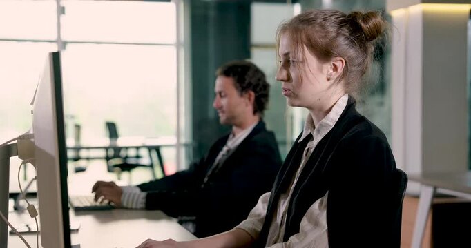 Female business professional typing at computer during office work session with male colleague nearby. Collaborative startup working scene focused on productivity and planning