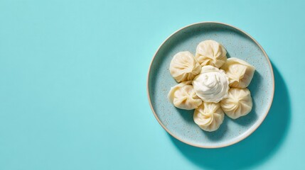 Top view of homemade dumplings arranged on ceramic plate with sour cream, minimal food styling on turquoise background.